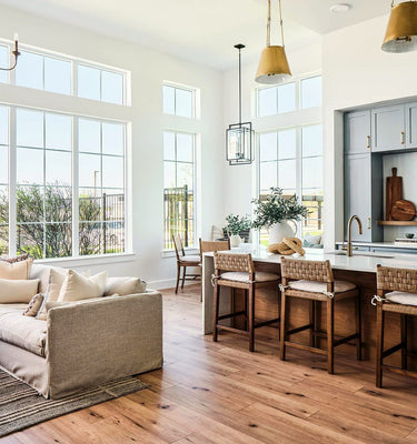 Bright open-plan living room and kitchen with a large island, bar stools, tall windows and warm wood floors